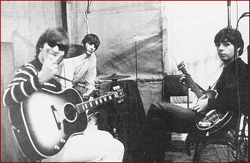 13: Take That! (In Stripes): At London’s Abbey Road Studios in 1965, John Lennon (left) makes a “digital” statement to the photographer. John is again wearing casual white pants and a black and white horizontal striped lightweight sweater. Ringo Starr (center) and Paul McCartney (far right) look on.